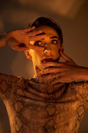 Eine junge queere Person in stylischer Kleidung hält sich die Hände vors Gesicht.