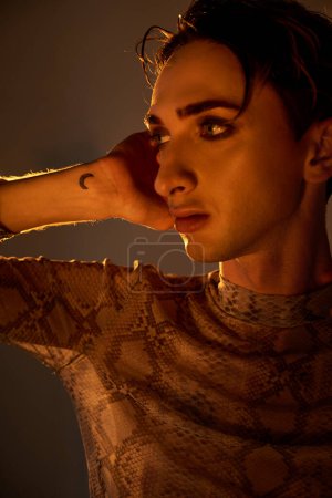 Eine junge queere Person in einem Oberteil aus Schlangenhaut posiert in stilvoller Manier von Selbstvertrauen und Stolz für die Kamera.