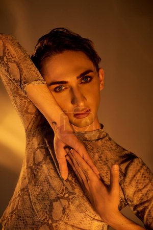 A young queer person confidently poses in a python skin dress, embodying style, identity, and pride.