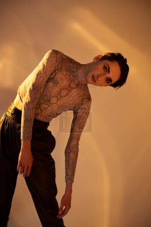Ein junger queerer Mann mit tätowiertem Körper posiert mutig vor weißem Hintergrund.
