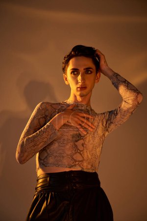 A young queer man with tattoos strikes a confident pose, hands on hips, showcasing her unique style and pride.