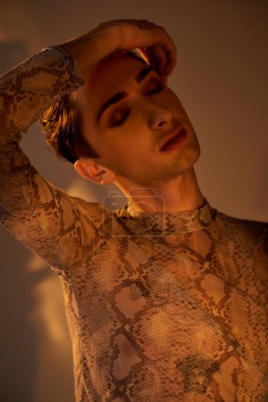 Téléchargez les photos : Jeune homme queer posant avec confiance dans une chemise élégante en peau de serpent, exprimant la fierté LGBT. - en image libre de droit