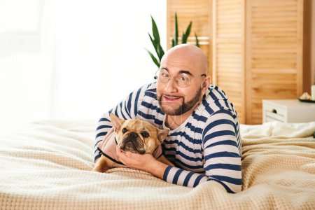 Ein Mann umarmt friedlich eine kleine französische Bulldogge, während er auf einem Bett liegt.