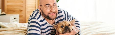 Stylish man in glasses cuddles small French bulldog at home.