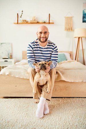 Photo for A man in glasses relaxes on bed while holding a French Bulldog. - Royalty Free Image