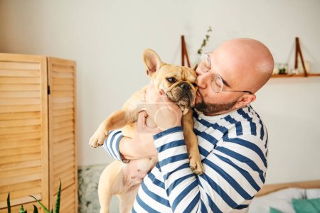 Foto de Hombre guapo con gafas acunando un pequeño Bulldog francés en sus brazos. - Imagen libre de derechos