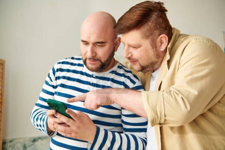 Two men, a gay couple, engrossed in their cell phone screen at home.
