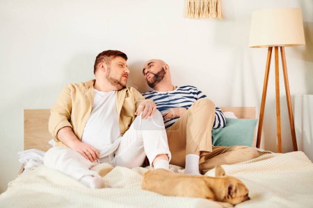 Téléchargez les photos : Un beau couple gay s'assoit confortablement sur un lit avec leur bouledogue français. - en image libre de droit