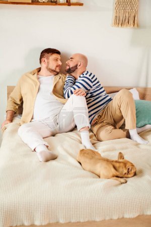 Two men laying on a bed with their French Bulldog beside them.
