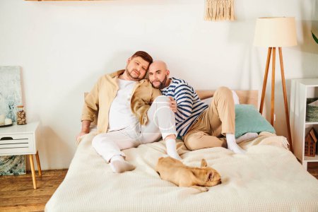 Una pareja gay y su bulldog francés descansando encima de una cama.