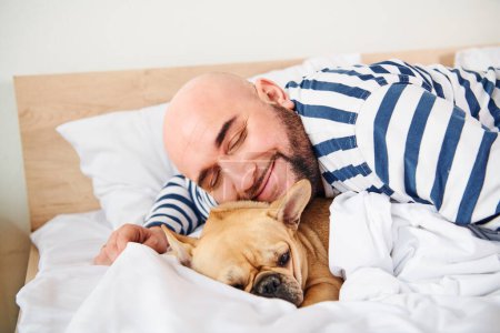 A man and his dog peacefully lie in bed together.