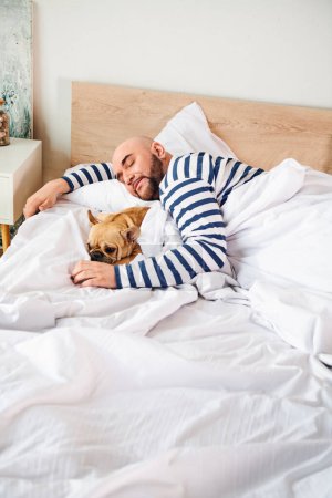 Foto de Un hombre y su adorable Bulldog francés se abrazan juntos en la cama. - Imagen libre de derechos
