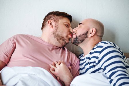 Téléchargez les photos : Un couple d'hommes couchés au lit partageant un baiser tendre. - en image libre de droit