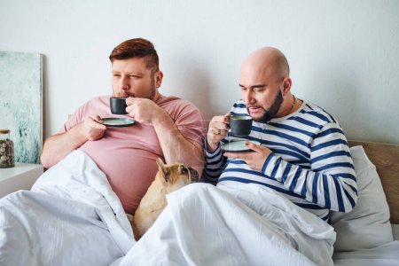 A couple of men and their French Bulldog sitting together on a bed, enjoying a peaceful moment.