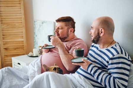 Téléchargez les photos : Un gay couple et leur français bouledogue se prélasser sur un lit. - en image libre de droit