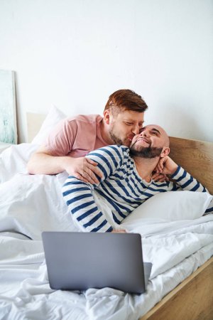 Foto de Dos hombres se acurrucan en la cama con un portátil. - Imagen libre de derechos