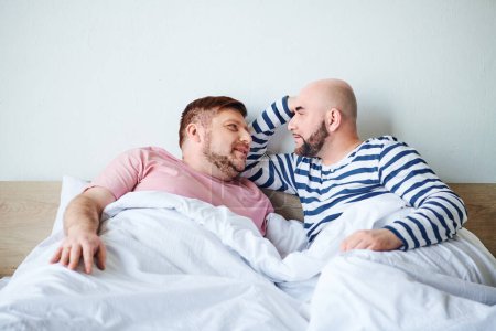 Téléchargez les photos : Une paire d'hommes couchés côte à côte au lit, passant du temps de qualité ensemble. - en image libre de droit