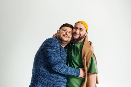 Two men hug in front of white background.