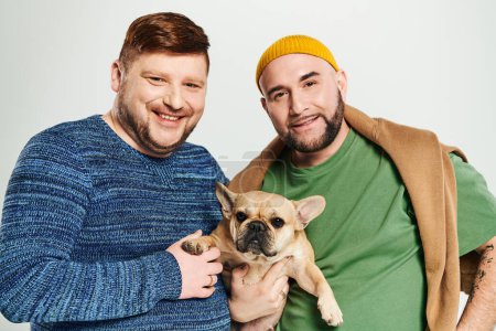 Zwei stilvolle, verliebte Männer posieren mit einer kleinen französischen Bulldogge.
