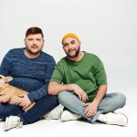Two men sit lovingly holding a French Bulldog.