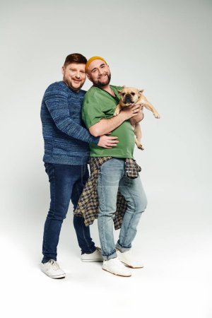 Foto de Una pareja gay amorosa de pie juntos, sosteniendo un bulldog francés. - Imagen libre de derechos