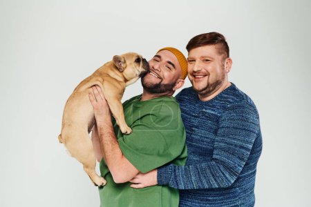 Photo for Two attractive men stand together with their French bulldog. - Royalty Free Image