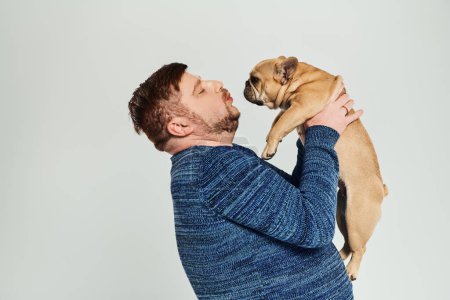 Foto de Un hombre con amor sostiene a un Bulldog francés frente a su cara. - Imagen libre de derechos
