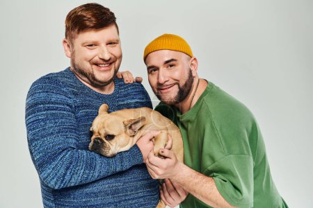 Two men tenderly hold a small French Bulldog in their arms.