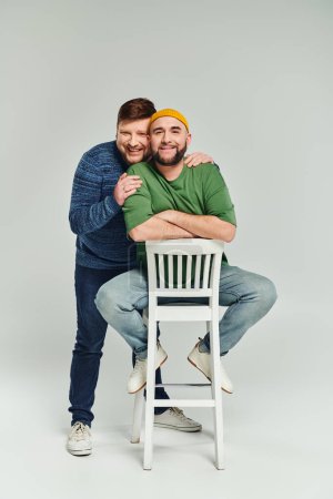 Téléchargez les photos : Deux hommes serrant affectueusement sur une chaise, mettant en valeur l'amour et la convivialité dans un moment intime. - en image libre de droit