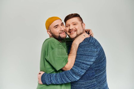 Two men hug warmly against a white backdrop.