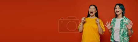Téléchargez les photos : Asiatique mère et adolescente fille debout côte à côte dans un studio sur un fond orange. - en image libre de droit