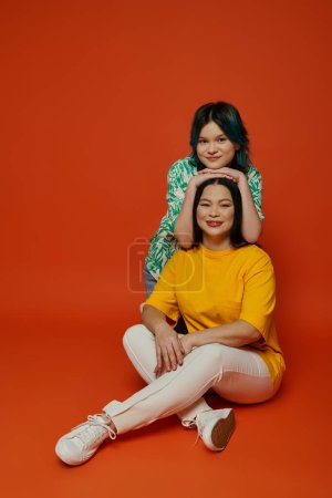 Téléchargez les photos : Une mère asiatique assise par terre à côté de sa fille adolescente, partageant un moment de proximité et de connexion. - en image libre de droit