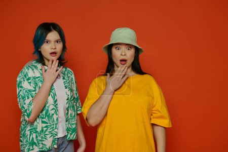 Téléchargez les photos : Une mère et sa fille adolescente, toutes deux asiatiques, se tiennent côte à côte dans un studio sur fond orange. - en image libre de droit