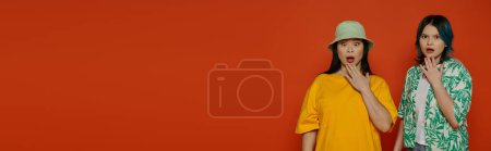 Téléchargez les photos : Two women, an Asian mother and her teenage daughter, stand gracefully in front of a bold red wall in a studio setting. - en image libre de droit