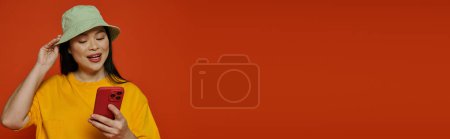 Téléchargez les photos : Une femme en chemise jaune tient un téléphone portable, se connectant avec quelqu'un par la technologie sur un fond orange. - en image libre de droit