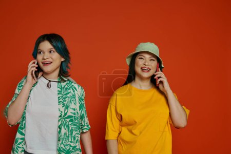 Téléchargez les photos : Une mère asiatique et sa fille adolescente debout l'une à côté de l'autre, absorbés dans des conversations téléphoniques séparées. - en image libre de droit