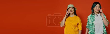 An Asian mother and her teenage daughter stand together in a studio against an orange background