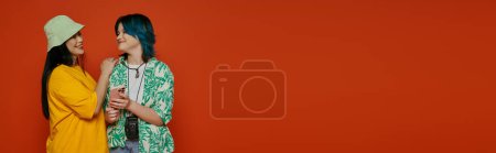Photo for A mother and her teenage daughter, both Asian, stand side by side in front of a bright red wall, showcasing a strong bond. - Royalty Free Image