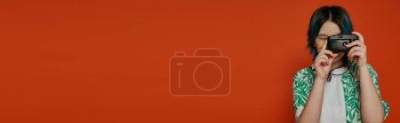 Téléchargez les photos : Adolescent fille prendre une photo avec un appareil photo dans un studio sur un fond orange. - en image libre de droit