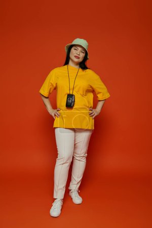 Téléchargez les photos : Une femme asiatique posant ensemble dans un studio, mettant en valeur leur chemise jaune élégante et pantalon blanc sur un fond orange. - en image libre de droit