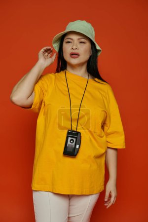 Téléchargez les photos : Une femme asiatique posant dans un studio, portant une chemise jaune et un chapeau vert. - en image libre de droit
