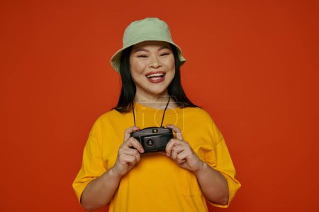 Una mujer asiática sostiene felizmente una cámara, sonriendo al espectador, en un estudio