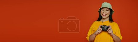 Foto de Una mujer con una camisa amarilla sostiene una cámara en un estudio sobre un fondo naranja. - Imagen libre de derechos