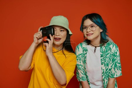 Photo for An Asian mother and her teenage daughter stand together in a studio, showcasing unity and familial bond on an orange background. - Royalty Free Image