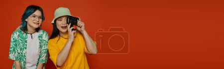 Photo for Asian mother and her teenage daughter standing side by side, both holding camera on an orange background. - Royalty Free Image