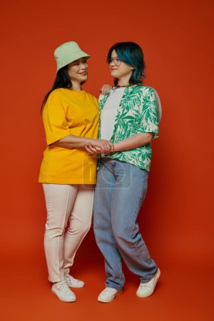 Téléchargez les photos : Une mère asiatique et sa fille adolescente se tiennent côte à côte, dégageant une énergie vibrante dans un studio sur fond orange. - en image libre de droit