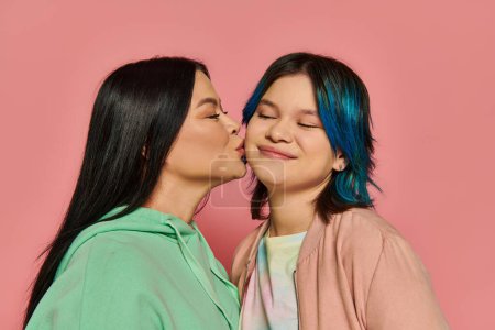 Téléchargez les photos : Mère et adolescente avec des cheveux bleus vibrants partagent un baiser tendre sur fond rose. - en image libre de droit