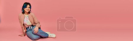 Téléchargez les photos : Une femme sereine en tenue décontractée assise paisiblement sur le sol sur un fond rose vif. - en image libre de droit