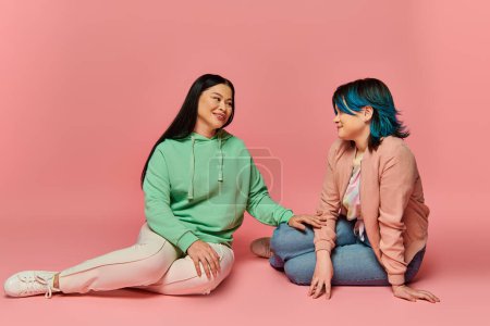 Two women, an Asian mother and her teenage daughter, sit on the ground engaged in a conversation, portraying closeness and connection.
