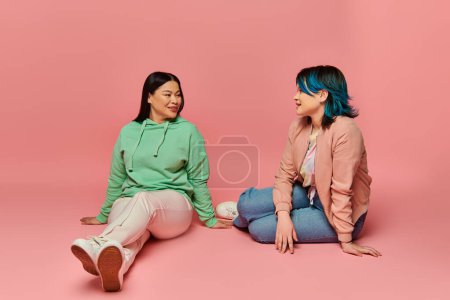 Foto de Una madre asiática y su hija adolescente vestida de manera casual, sentadas en el suelo, entablando una conversación profunda. - Imagen libre de derechos
